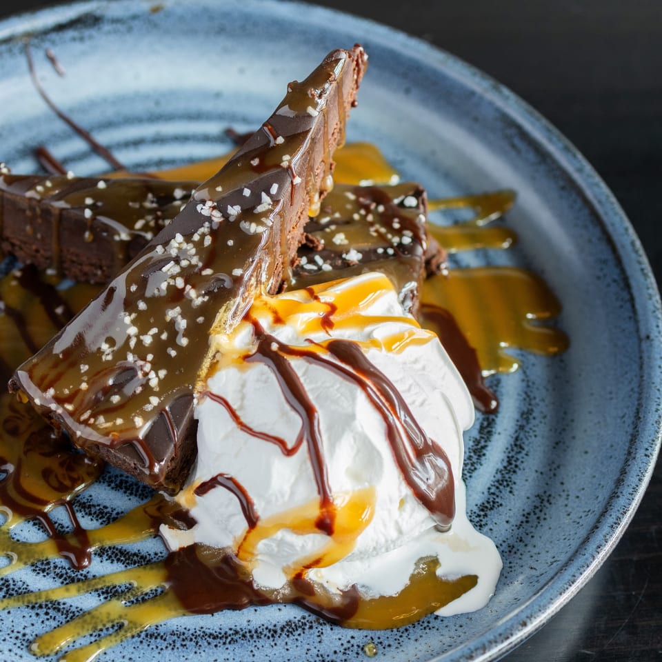 Chocolate brownie wedges topped with whipped cream, caramel and chocolate sauce, sprinkled with chopped nuts on a blue plate.